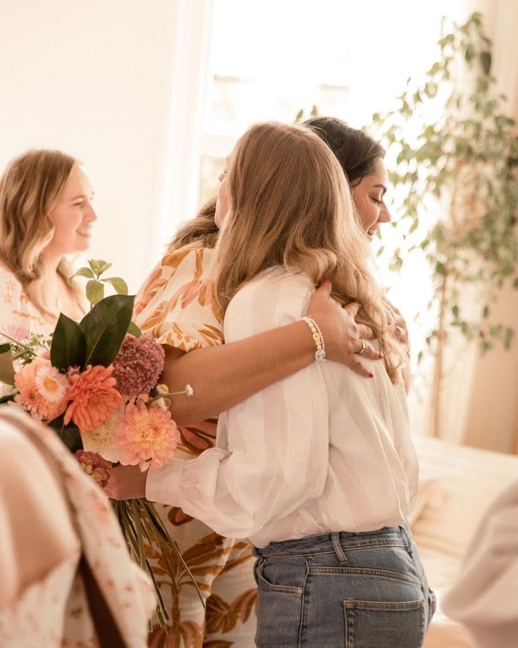 Mulheres se abraçando em um encontro, com um buquê de flores ao lado